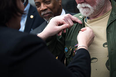 Kim Joiner, the acting principal deputy assistant to the secretary of defense for public affairs, pins a Vietnam veteran lapel pin on a veteran during an observance of Vietnam War Veterans Day at the Vietnam War Memorial in Washington